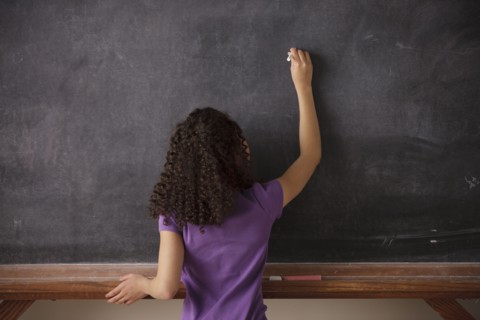 Portrait of schoolgirl (10-11) writing on blackboard. 
Photo : Rob Lewine