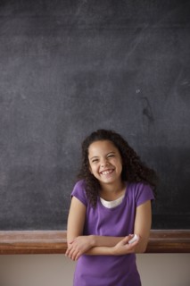 Portrait of schoolgirl (10-11) standing in front of blackboard. 
Photo : Rob Lewine