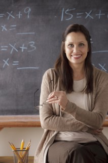 Portrait of teacher in classroom holding glasses. 
Photo : Rob Lewine