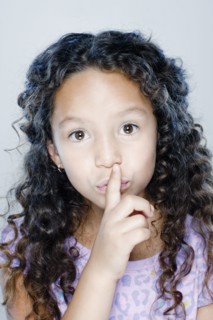 Portrait of girl (8-9) with finger on her lips, studio shot. 
Photo : Rob Lewine
