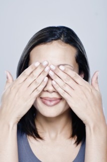 Portrait of young woman with hands covering eyes, studio shot. 
Photo : Rob Lewine