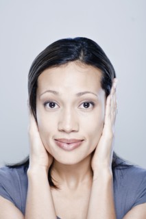 Portrait of young woman with hands covering ears, studio shot. 
Photo : Rob Lewine