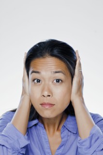 Portrait of young woman with hands covering ears, studio shot. 
Photo : Rob Lewine