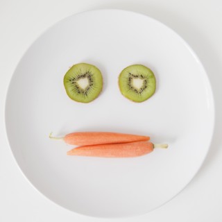Fruit and vegetable face on plate, studio shot. 
Photo : Jessica Peterson
