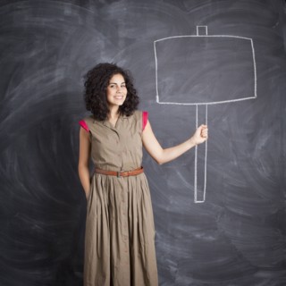 Young teacher posing against blackboard with blank banner written in chalk. 
Photo : Jessica