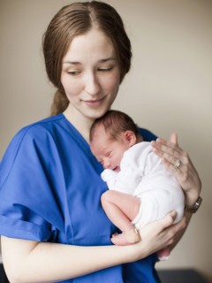 Portrait of young female nurse holding baby boy (2-5 months). 
Photo : Jessica Peterson