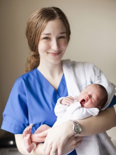 Portrait of young female nurse holding baby boy (2-5 months). 
Photo : Jessica Peterson