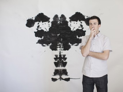 Man looking standing in front of complex shape painted on wall. 
Photo : Jessica Peterson