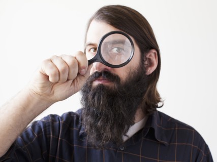 Bearded young man looking through magnifying glass. 
Photo : Jessica Peterson