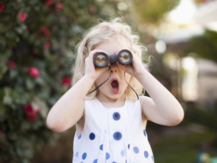 Surprised young girl (4-5) looking through binoculars. 
Photo : Jessica Peterson