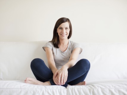 Happy young woman sitting on bed. 
Photo : Jessica Peterson