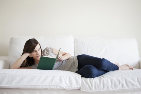 Young woman reclining on bed, reading book. 
Photo : Jessica Peterson