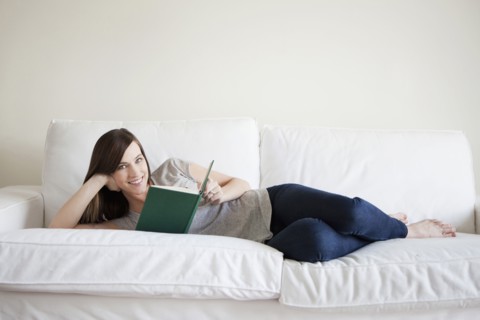 Young woman reclining on bed, reading book. 
Photo : Jessica Peterson