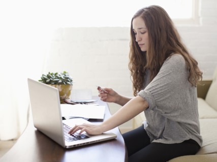 Young attractive woman using laptop while sitting on sofa. 
Photo : Jessica Peterson