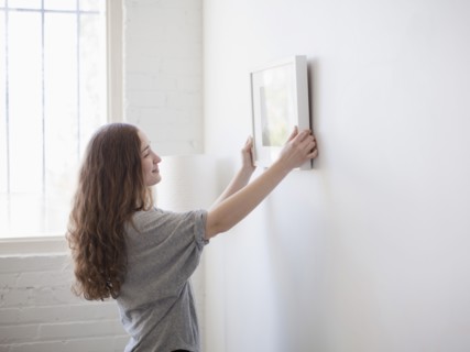 Young woman hanging picture on freshly painted wall. 
Photo: Jessica Peterson