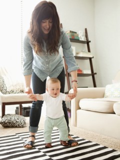 Young mother assisting baby boy (6-11 months) in his first steps. 
Photo : Jessica Peterson