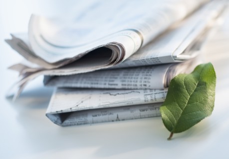 Studio shot of newspaper and green leaf.