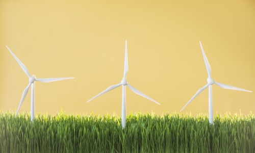 Model wind turbines in grass on yellow background.