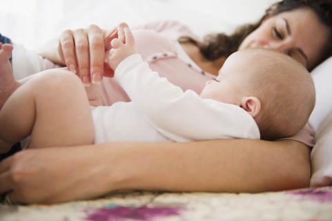 Mother and baby boy (2-5 months) lying together on bed. Photo : Jamie Grill