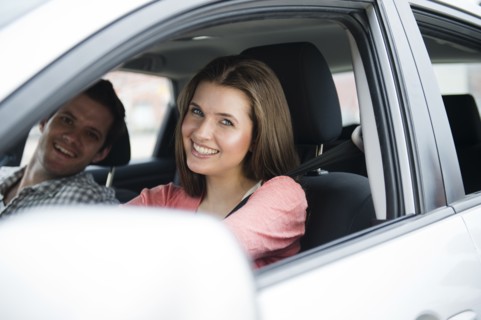 Happy young couple sitting in car. Photo: Jamie Grill