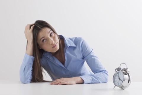 Studio shot of woman waiting by alarm clock. Photo: Jan Scherders