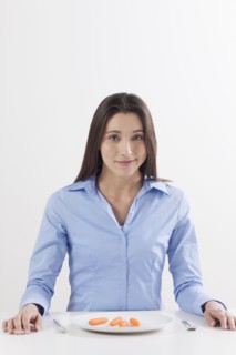 Studio shot of woman with baby carrots on plate. Photo : Jan Scherders