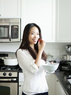 Portrait of smiling young woman eating strawberry in kitchen. Photo : Jessica Peterson