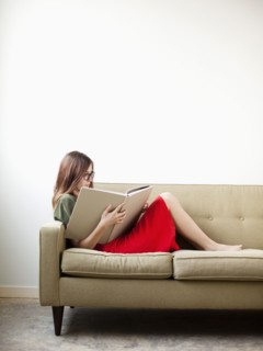Young woman on sofa reading book. Photo : Jessica Peterson