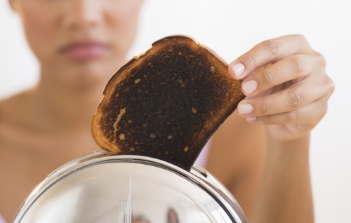 Woman taking burnt toast from toaster.