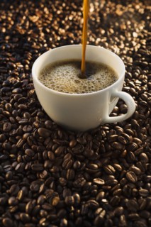 Pouring coffee into cup on coffee beans, studio shot.