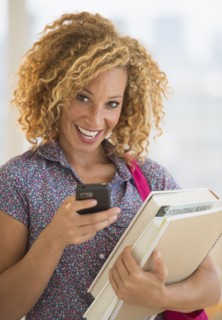 Young woman carrying books and using mobile phone.