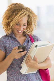 Young woman carrying books and using mobile phone.