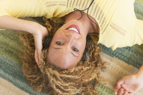 Young woman lying on carpet and listening to music on headphones.