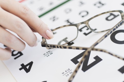 Close up of woman's hands holding glasses above eye chart, studio shot.
