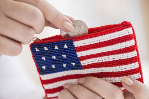 Woman holding coins and purse with american flag on it.