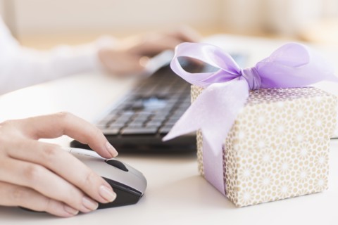 Gift box on desk next to woman using computer.