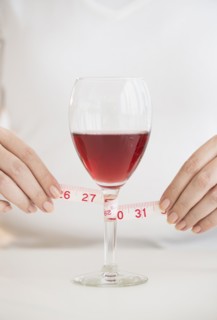 Woman measuring glass with rose wine.