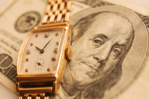 Studio shot of banknote and gold watch.