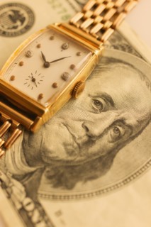 Studio shot of banknote and gold watch.