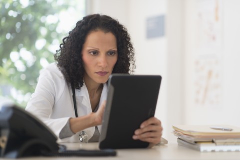 Portrait of doctor sitting in office and using digital tablet.