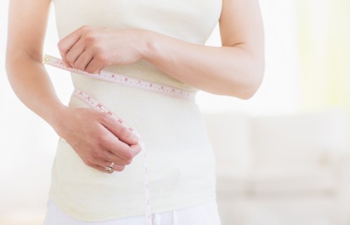 Young woman with tape measure wrapped around waist, midsection. Photo: Daniel Grill