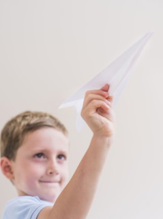 Young boy (6-7) playing with paper plane. Photo : Daniel Grill