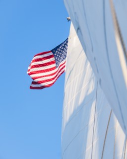 White sails and American flag against blue sky. Photo : Daniel Grill