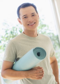 Happy mid adult man holding exercising mat. Photo : Daniel Grill