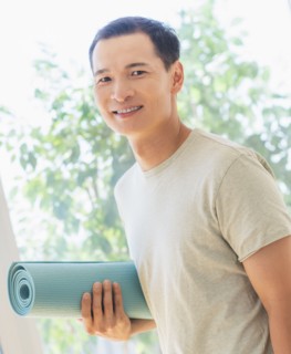 Happy mid adult man holding exercising mat. Photo : Daniel Grill