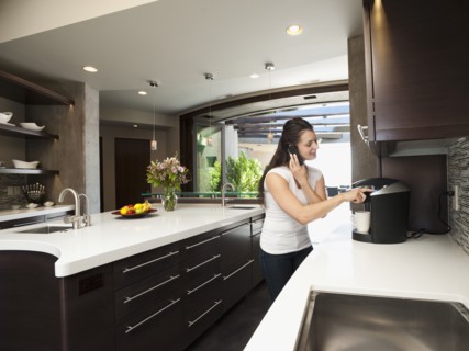 Young woman making morning coffee while using mobile phone.