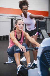 Woman exercising on row machine supervised by her trainer.