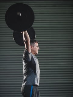 Mature man lifting heavy barbell .