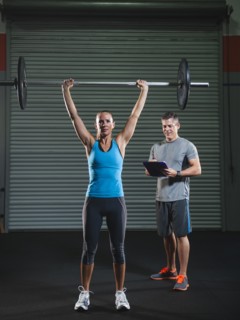 woman lifting barbell supervised with her trainer.