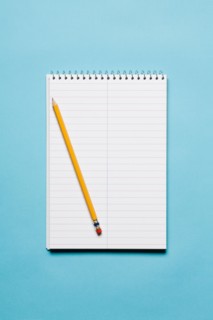 Single yellow sharpened pencil with blank stenographer notebook on blue background. Photo : Kristin